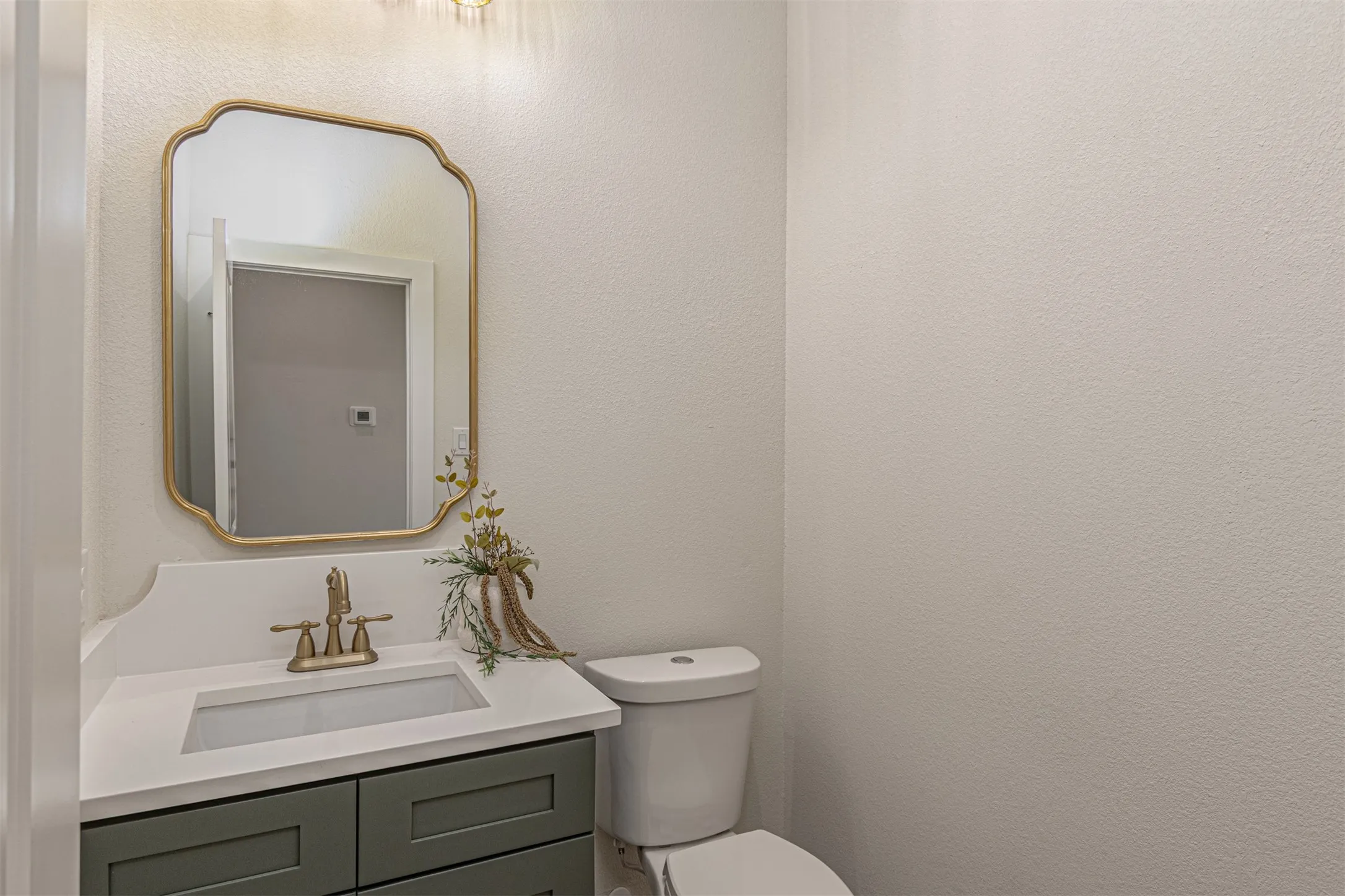 Powder room featuring a sage green vanity with white countertop, integrated sink, and brass-finish fixtures