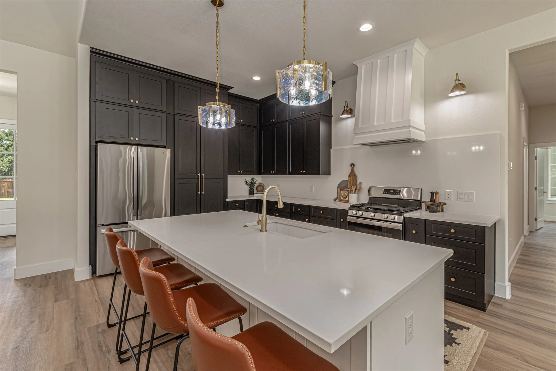 Gourmet kitchen featuring a large central island with seating, dark shaker-style cabinetry, white countertops, stainless steel appliances, and wood-finish flooring