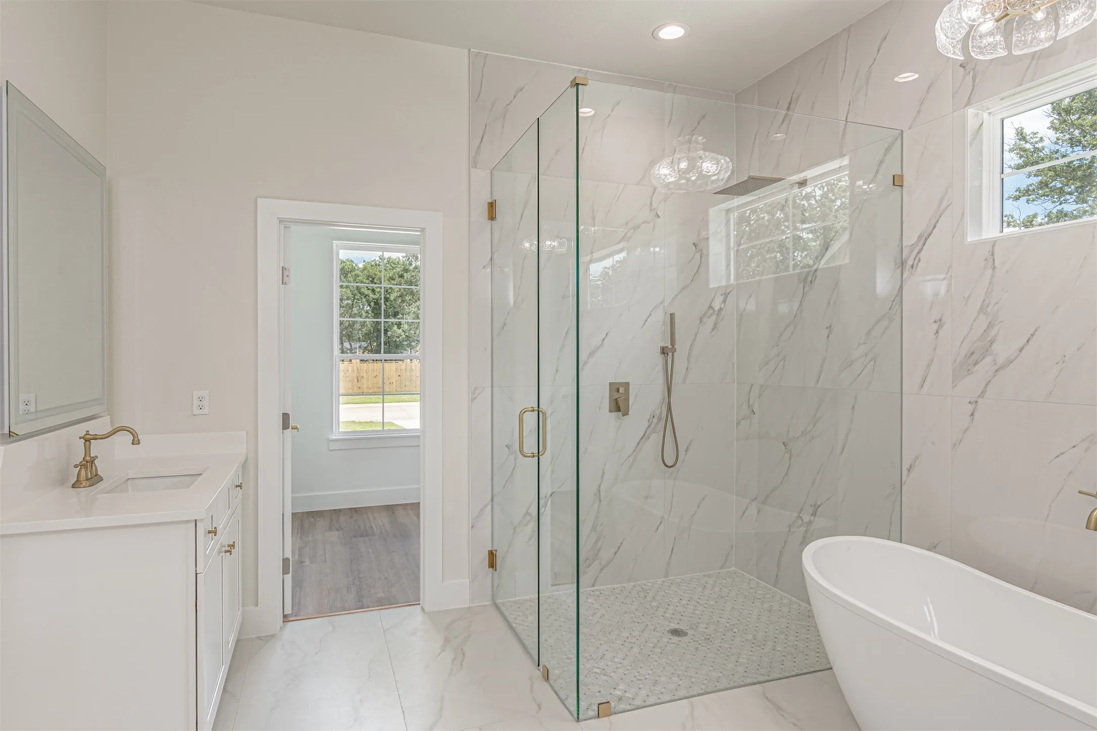 Spacious bathroom featuring a frameless glass shower enclosure, a freestanding soaking tub, and a white vanity with a rectangular sink