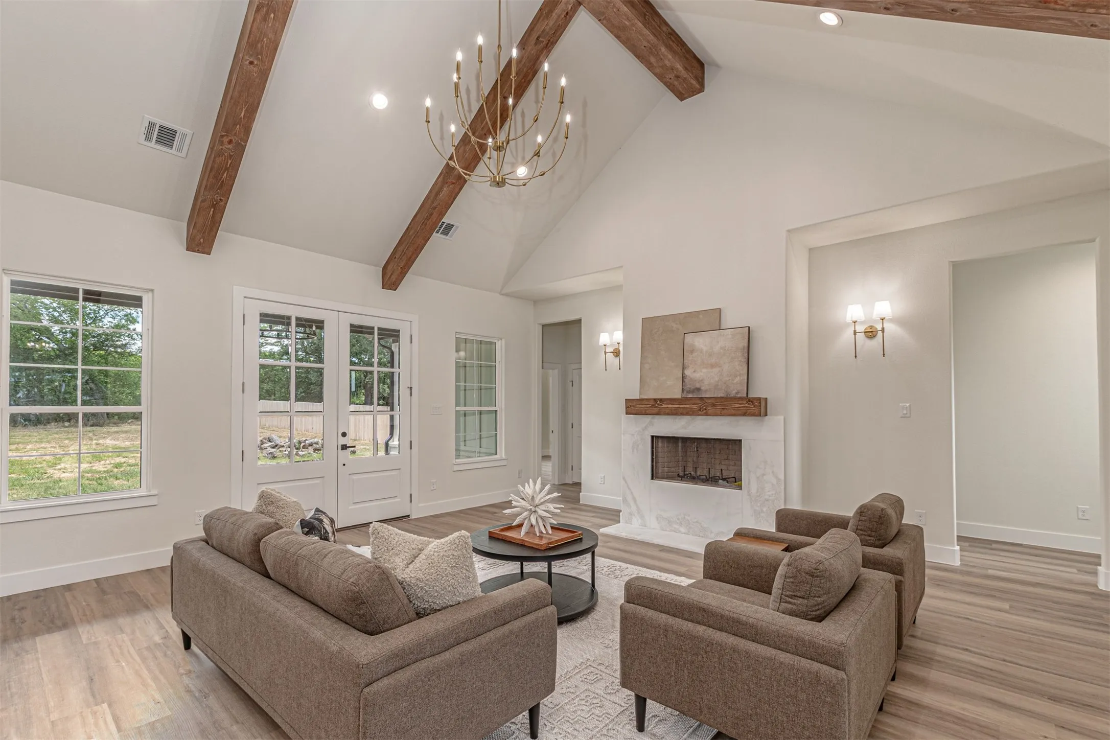 Spacious living area featuring a vaulted ceiling with exposed wood beams, a central chandelier, and wood-finish flooring