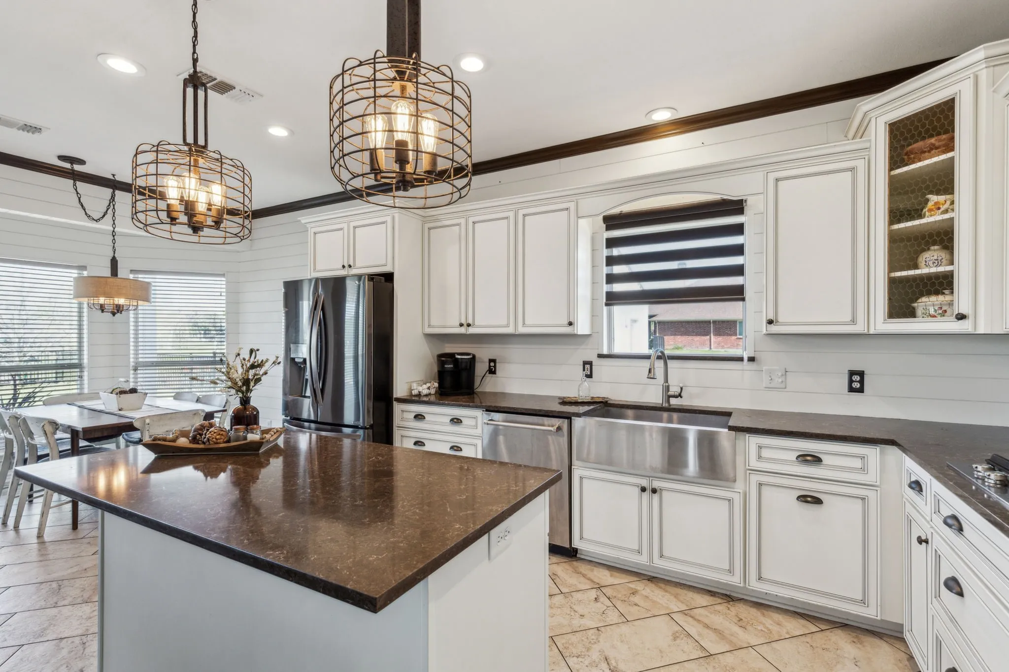 Beautifully updated kitchen with quartz countertops, tile floors, white cabinetry, stainless steel appliances, a large farm sink, and stylish light fixtures.