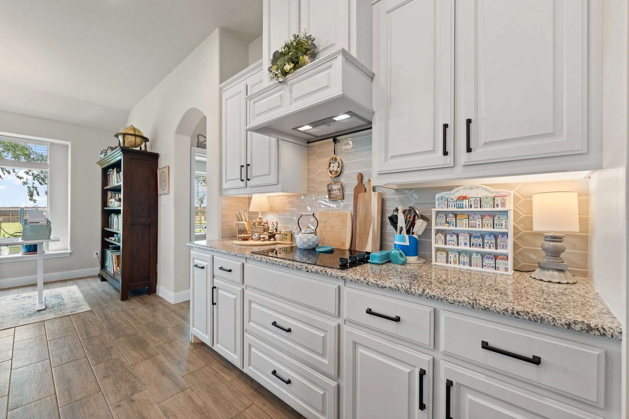 Kitchen featuring extensive white cabinetry with matte black hardware, speckled granite countertops, and a subway tile backsplash