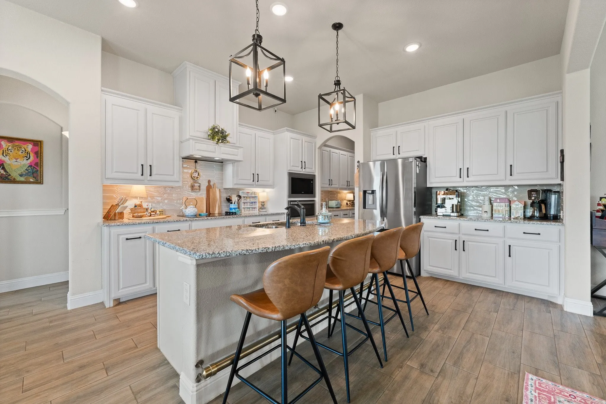 Open-concept kitchen featuring an oversized island with granite countertops, white cabinetry, integrated stainless steel appliances, and wood-finish flooring