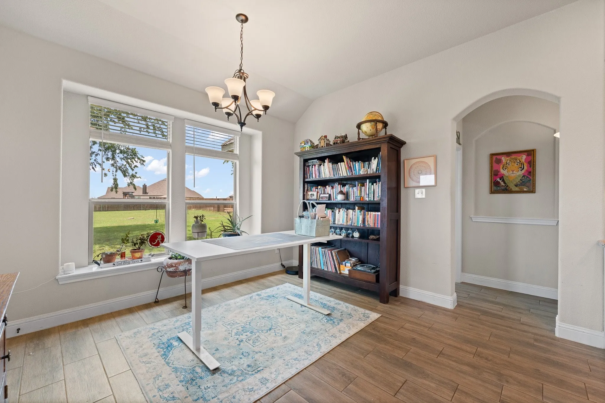 Vaulted ceiling room featuring a large window, a dark wood-finish bookcase, wood-finish flooring, a decorative chandelier, and an arched doorway