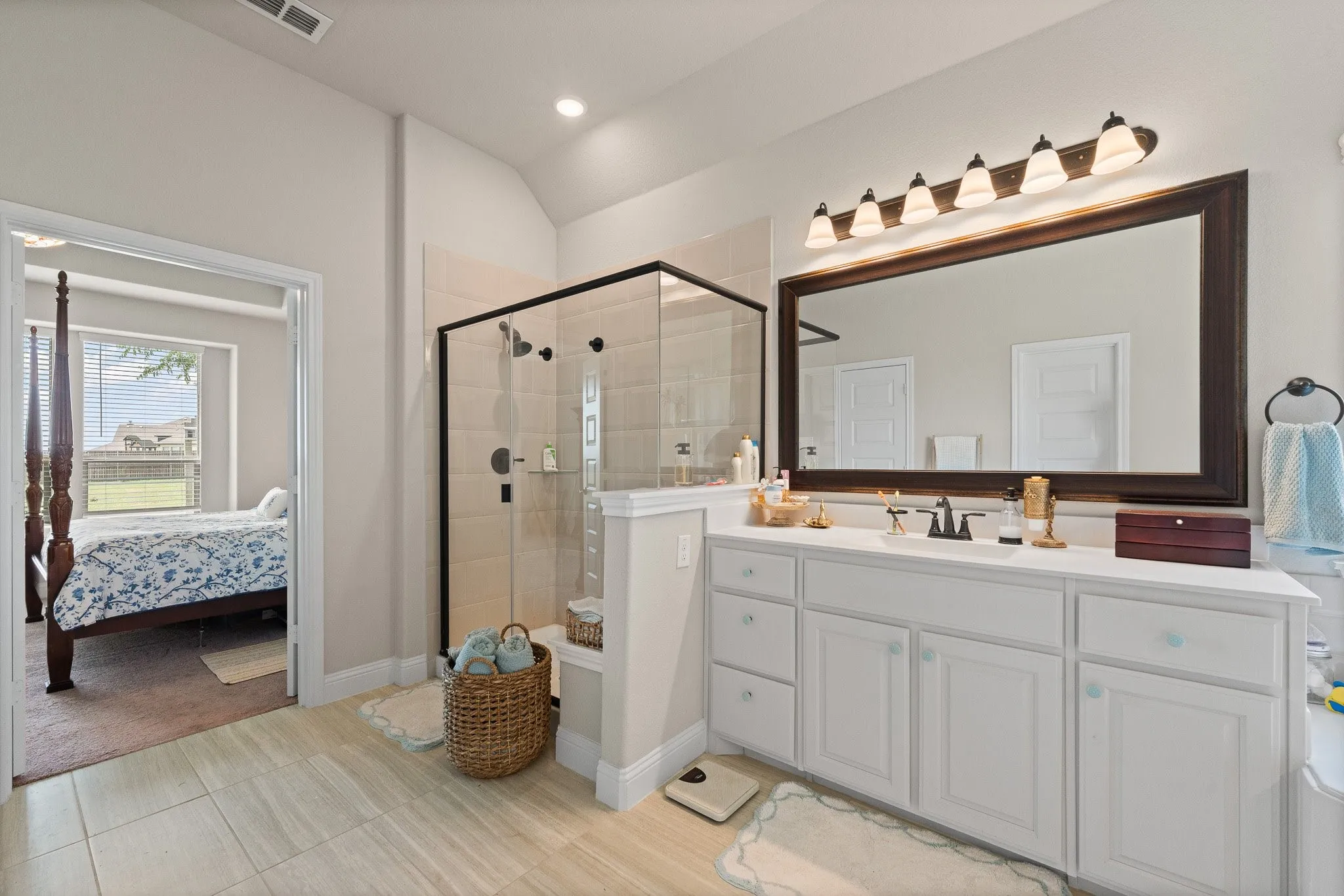 Spacious bathroom featuring a dual vanity with white cabinetry, a large framed mirror, and a walk-in shower with clear glass enclosure and tile surround