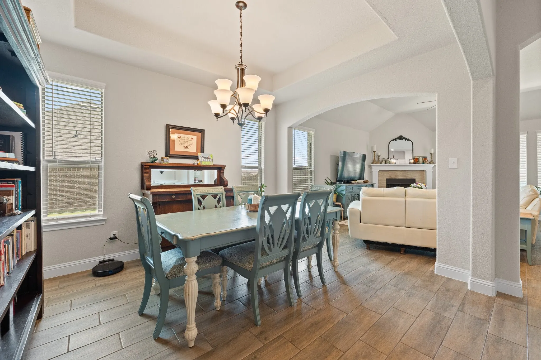Dining area featuring tray ceiling, chandelier lighting, wood-finish flooring, and an arched entry to a living space with a fireplace