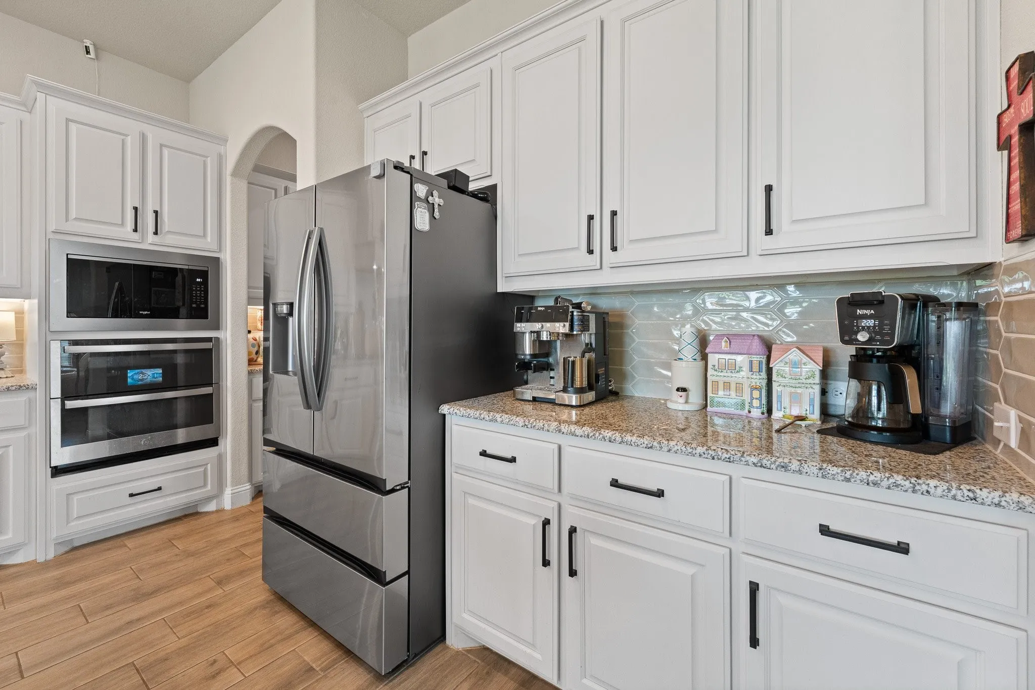 Kitchen featuring white cabinetry, stainless steel appliances, speckled countertops, a patterned tile backsplash, and wood-finish flooring