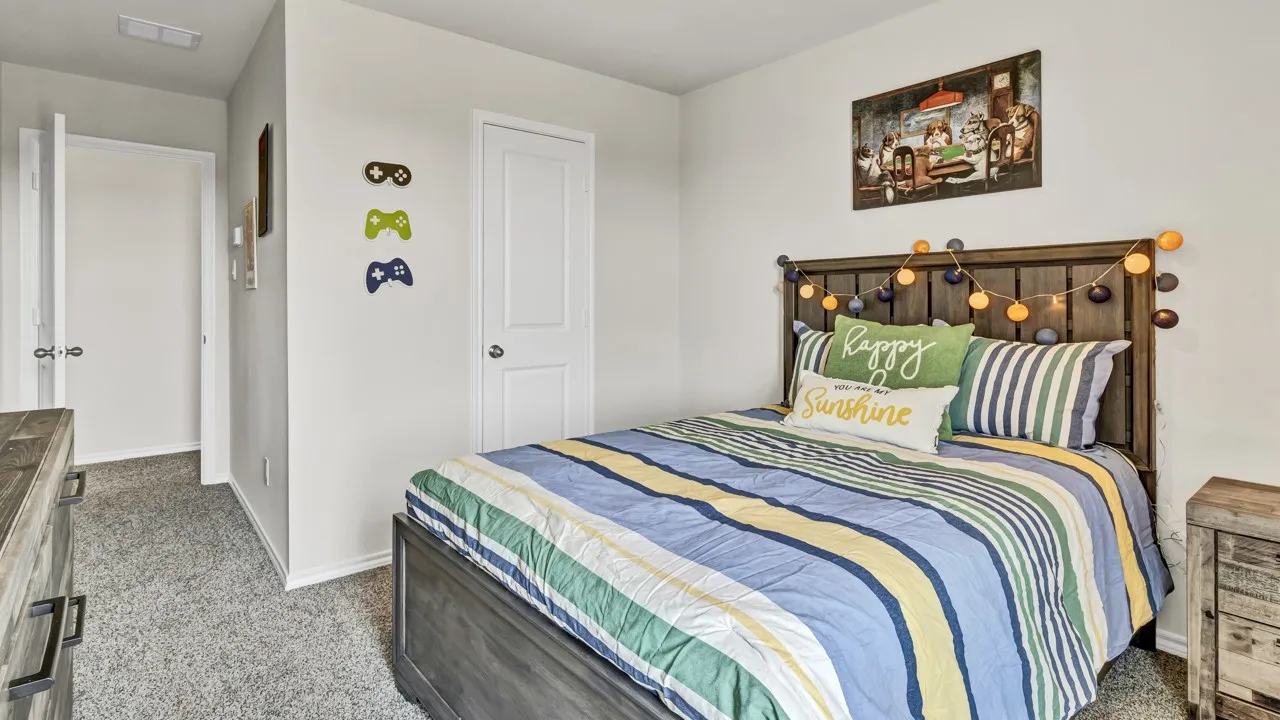 Bedroom featuring neutral wall paint, gray textured carpeting, a solid-panel door, baseboard trim, and a wood-finish bed frame with headboard