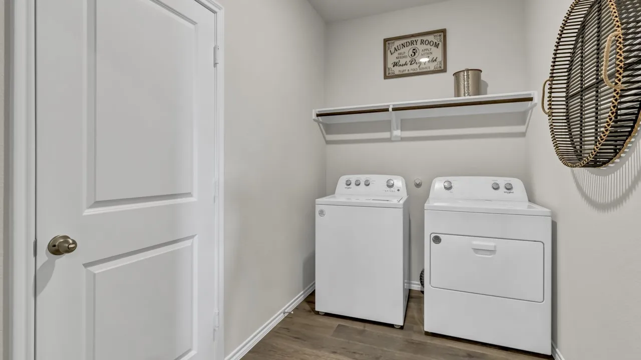 Dedicated laundry area featuring a white door with brass hardware, wood-finish flooring, and a wall-mounted shelf above the appliances