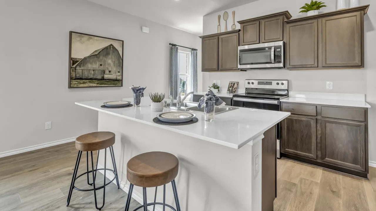 Kitchen featuring a white countertop island with an undermount sink, warm wood-finish flooring, dark wood cabinetry, a stainless steel microwave, and a black electric range