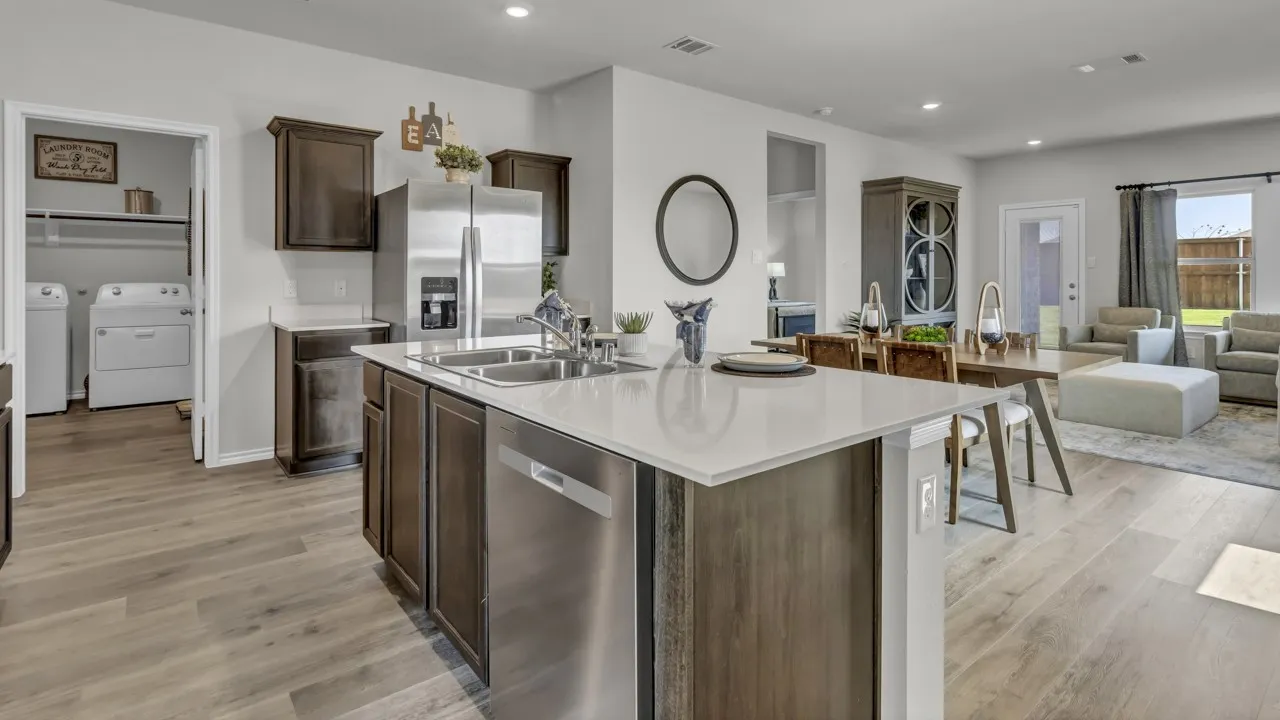 Open-concept living space featuring wood-finish flooring, a kitchen island with a double basin sink, stainless steel appliances, dark wood cabinetry, and recessed lighting