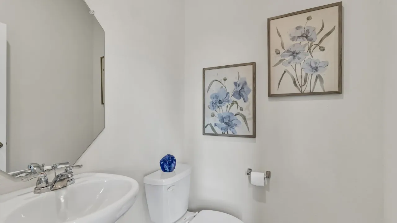 Bathroom featuring a pedestal sink with chrome fixtures, a modern toilet, and a geometric mirror