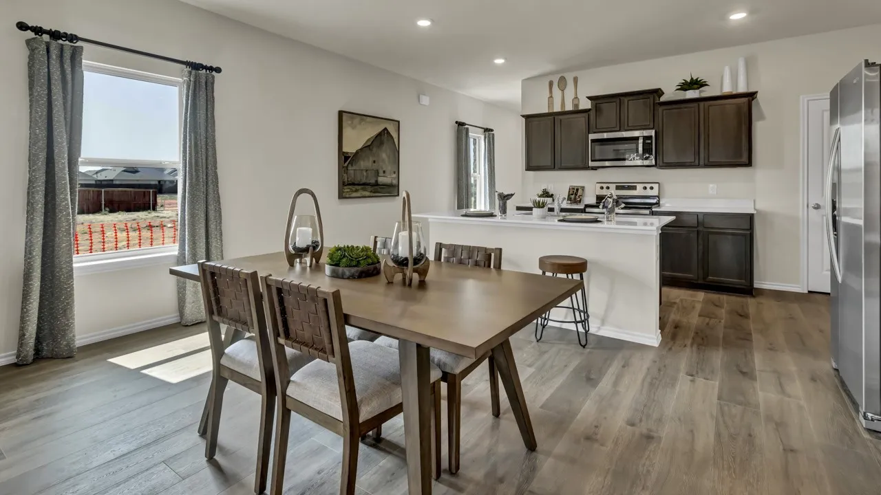 Open-concept dining area featuring wood-finish flooring, a contemporary window with drapes, a kitchen with dark cabinetry, stainless steel appliances, and a breakfast bar with a white countertop