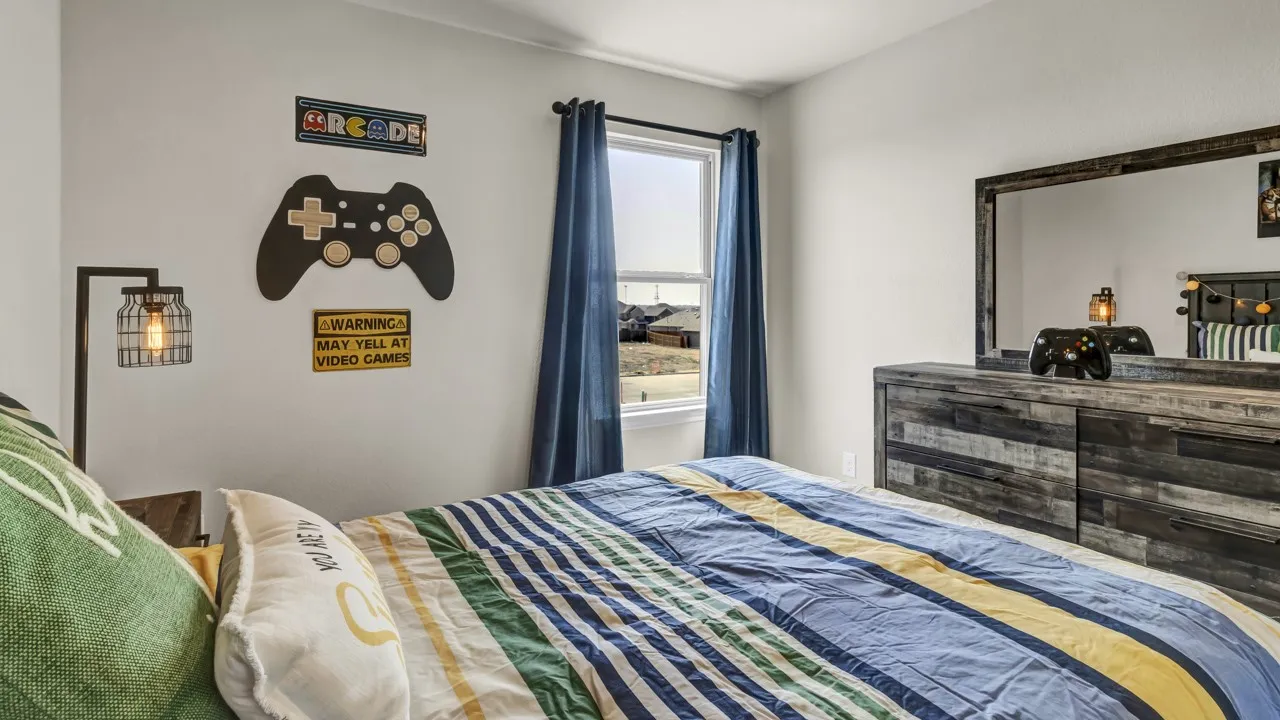 Bedroom featuring a single window with blue drapes, a wood-finish dresser with a mirror, and a wall-mounted industrial style light fixture