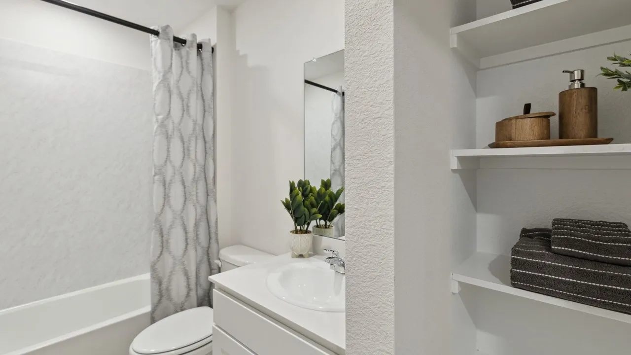 Bathroom featuring a white bathtub with a textured surround, a white vanity with an integrated sink, a large wall-mounted mirror, and built-in shelving