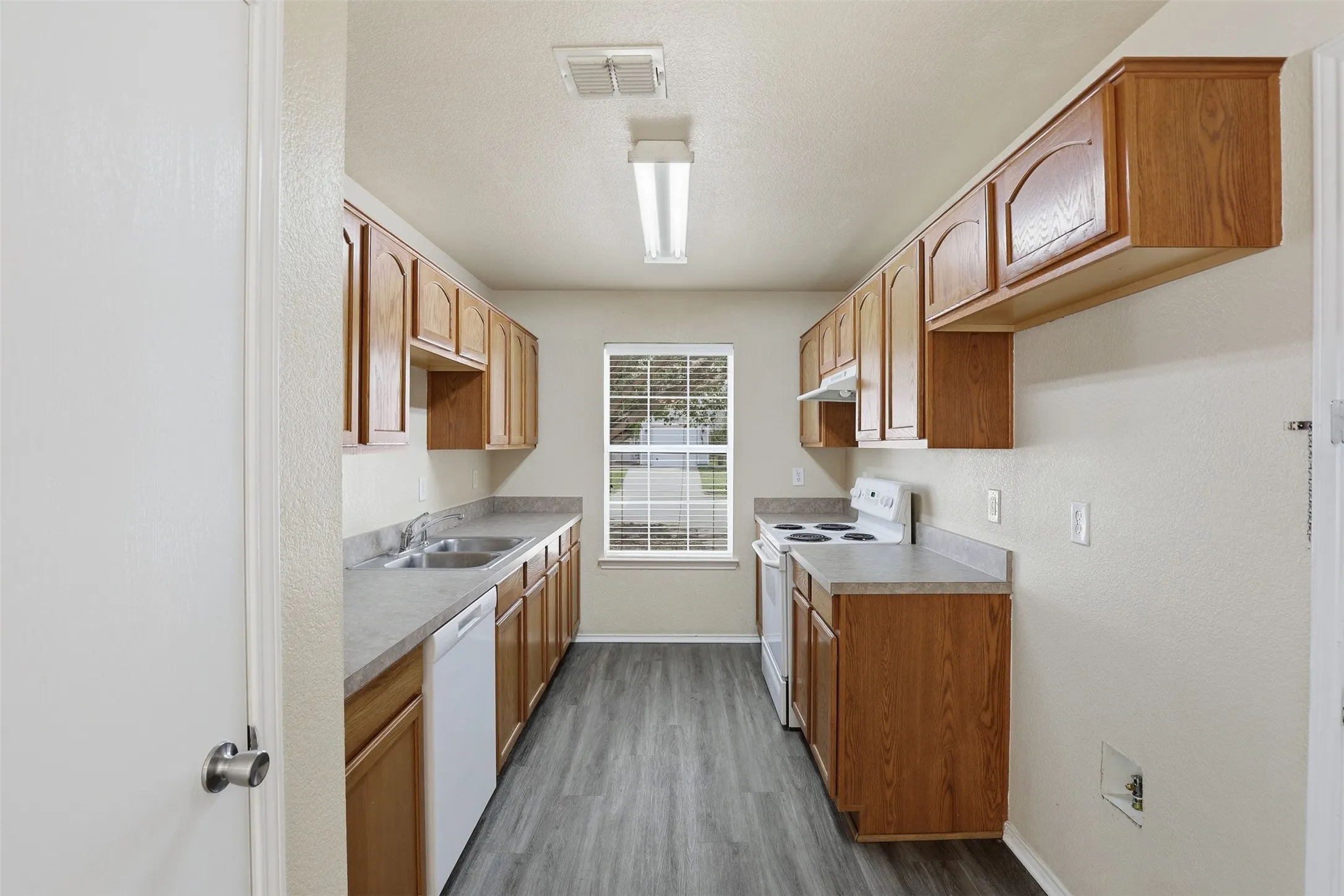 Galley kitchen featuring wood-finish cabinetry, laminate countertops, and wood-finish flooring