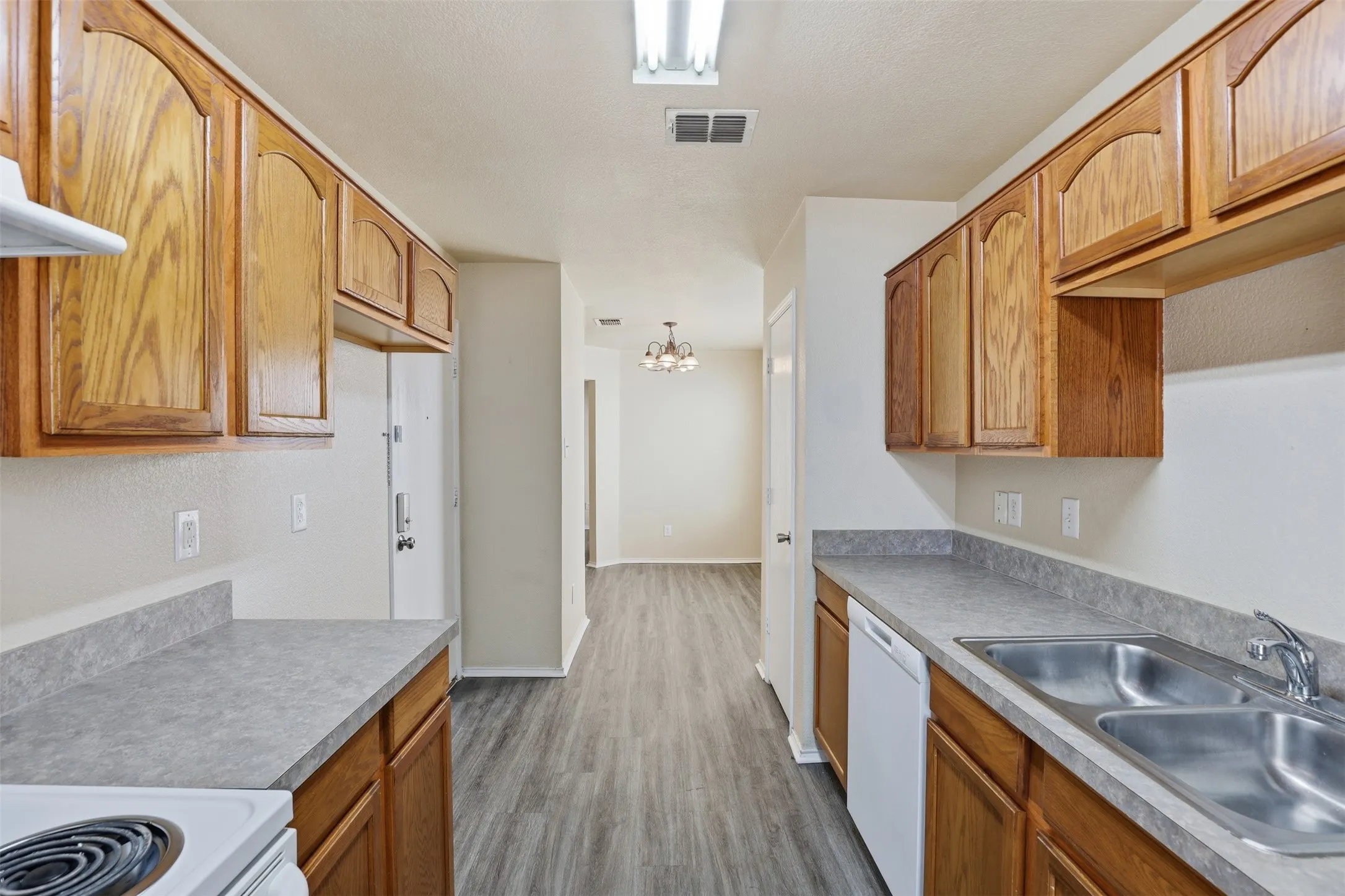 Galley kitchen featuring wood cabinetry, laminate countertops, a dual basin stainless steel sink, and wood-finish flooring