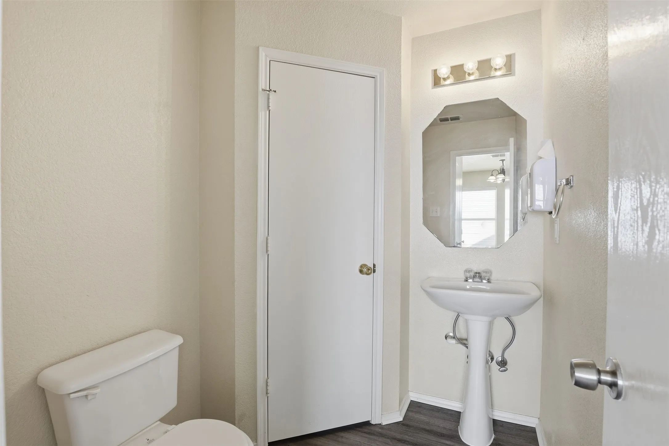 Bathroom featuring wood-finish flooring, a white pedestal sink with a chrome faucet, and an octagonal wall-mounted mirror
