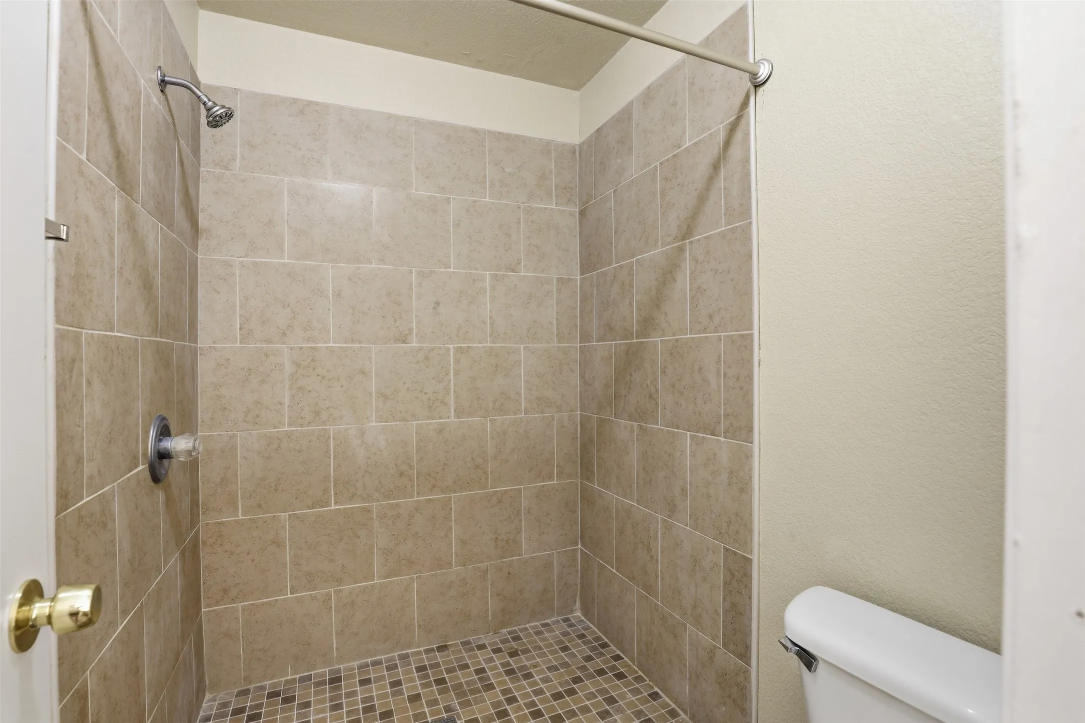 Shower enclosure featuring neutral-toned rectangular wall tiles, a mosaic tile shower pan, and a chrome shower head with coordinating hardware