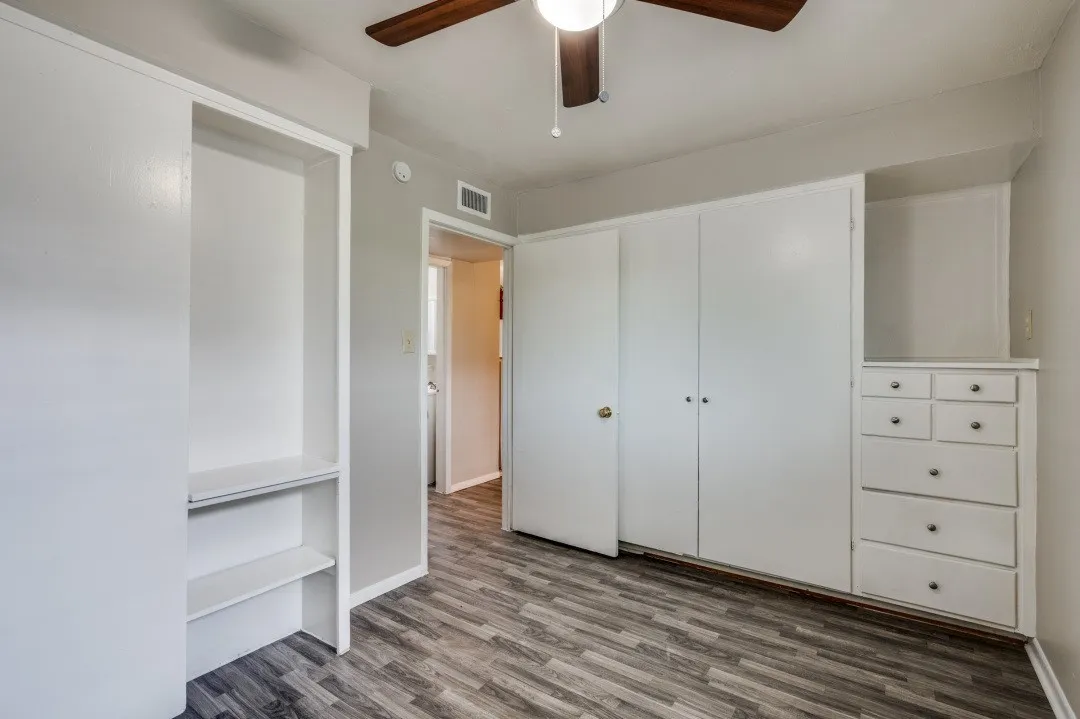 Wood-finish flooring with built-in cabinetry featuring shelving, drawers, and wardrobe doors
