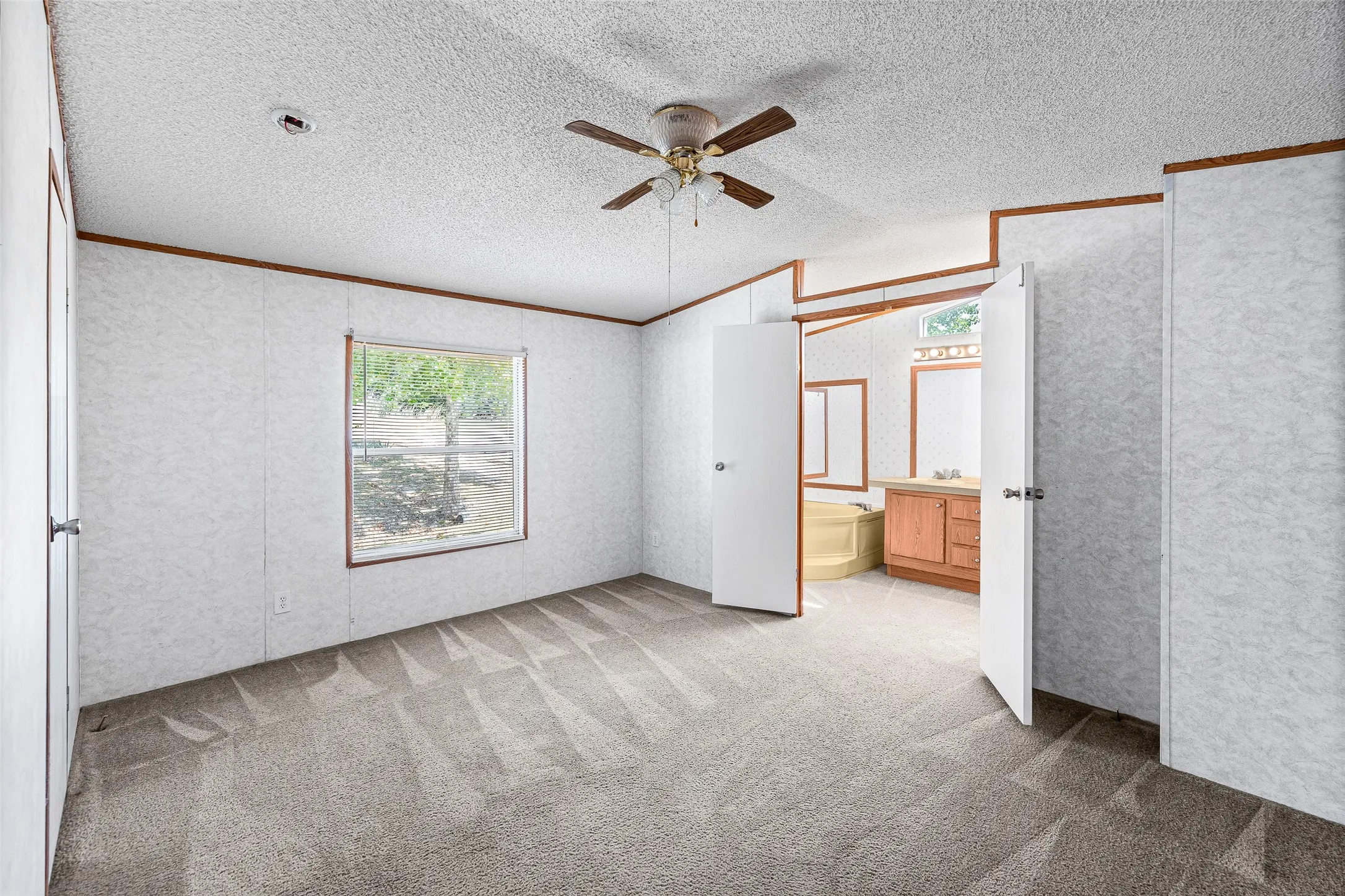 Carpeted room with a ceiling fan, a window, and direct access to a bathroom featuring a vanity with a sink and a built-in tub