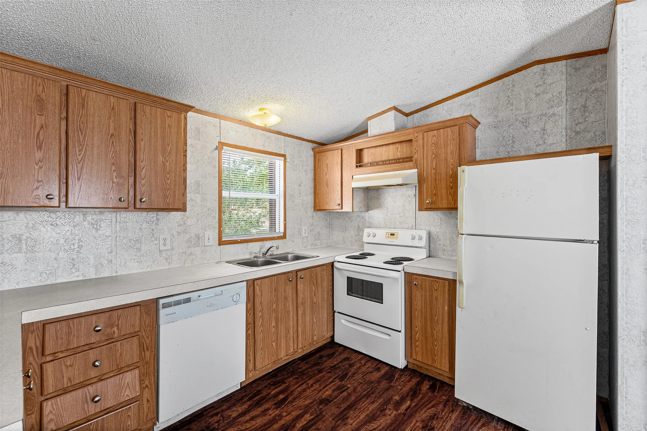 Kitchen featuring wood-finish cabinetry, white appliances, dual basin sink, and a window