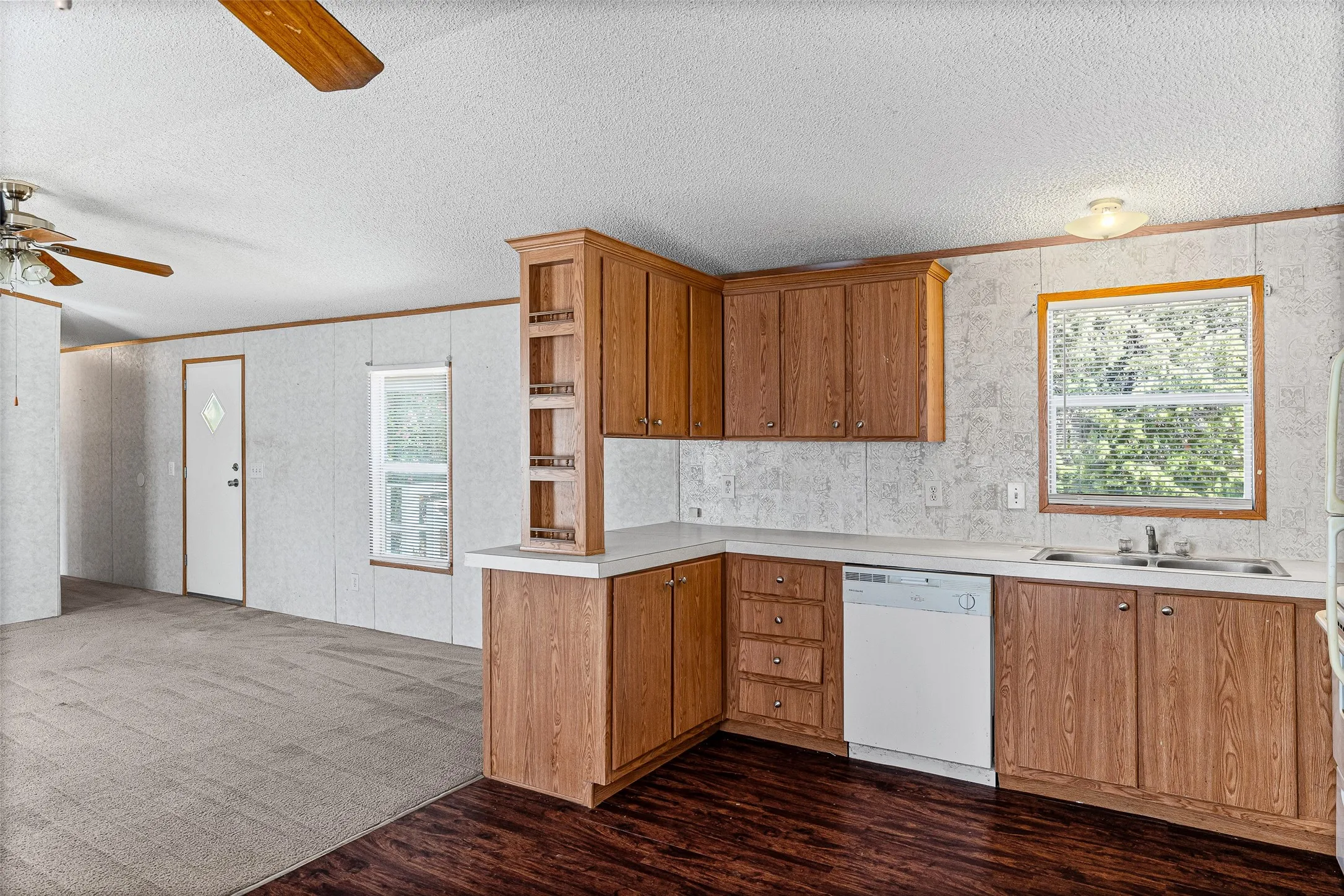 Kitchen with wood-finish cabinetry, white countertops, stainless steel sink, and white dishwasher