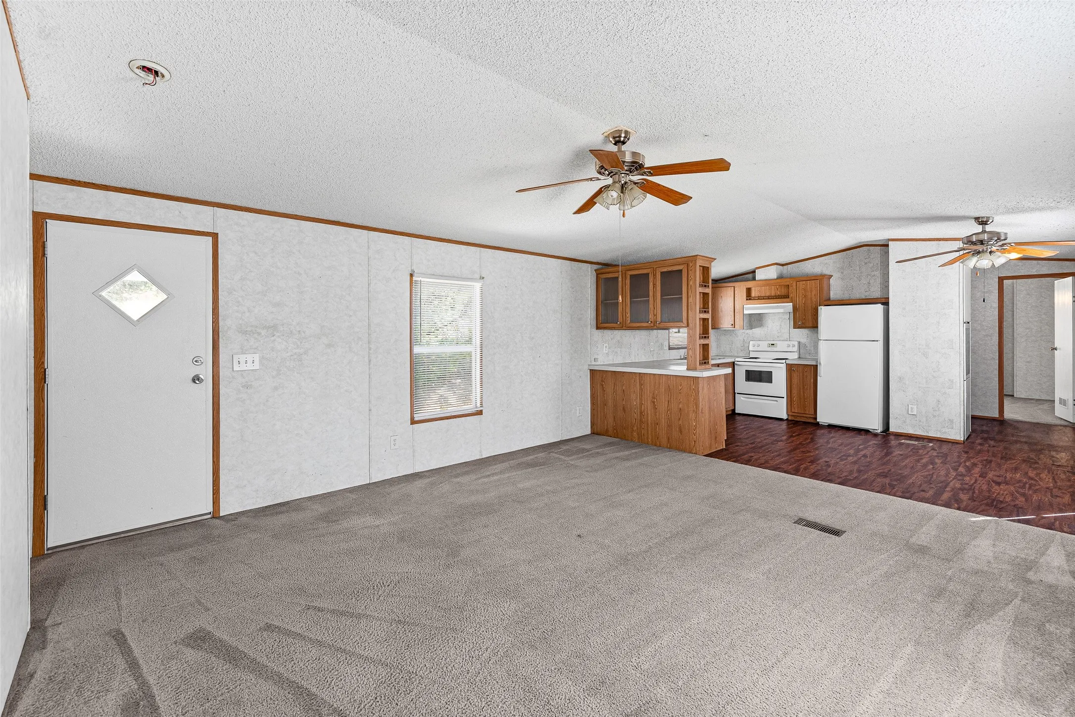 Open-concept living area featuring a kitchen with wood-finish cabinetry, white appliances, and a breakfast bar