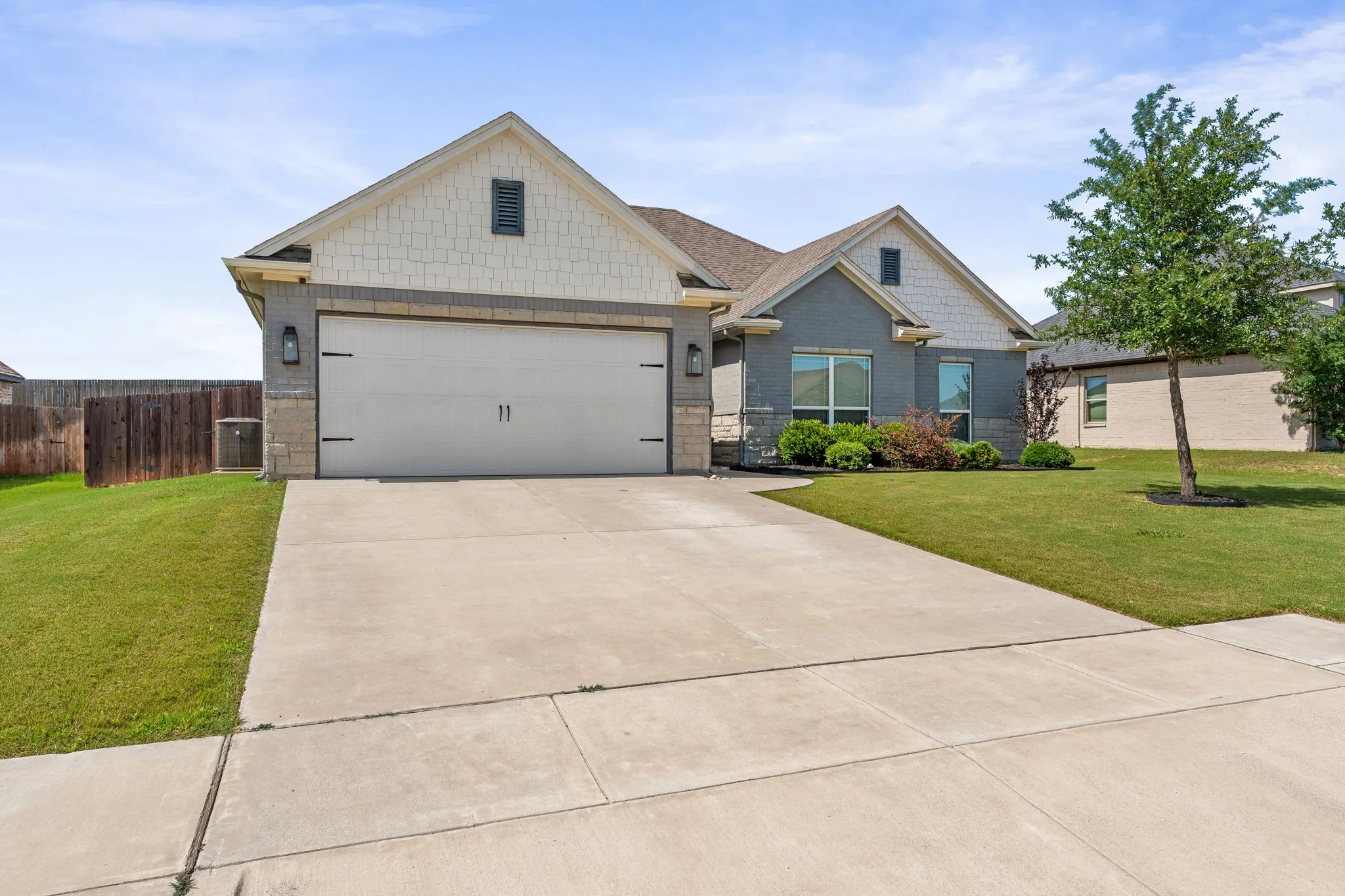 View of front of home, 2 car garage and driveway. Gray painted brick exterior around house with white painted shingle style siding.