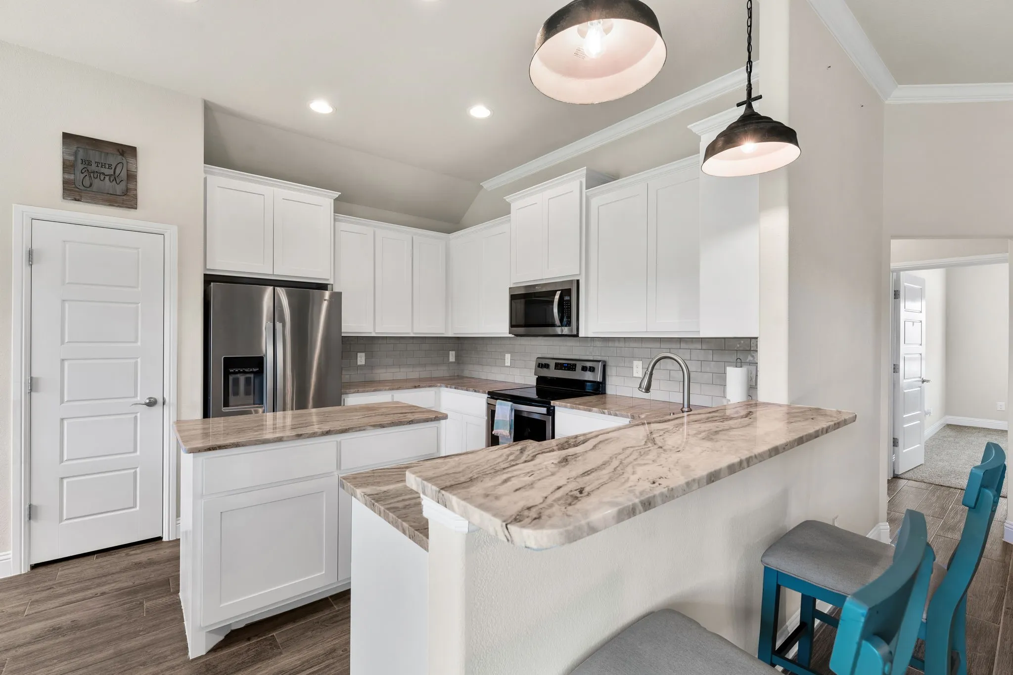 Kitchen with quartz countertops, white fresh white painted cabinetry, pantry, stainless fridge, range, and microwave, dishwasher.