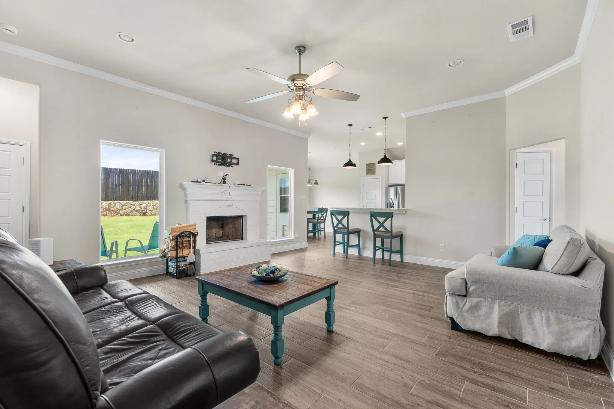 Living Room with ceiling fan, white painted brick wood burning fire place, windows for natural lighting, breakfast bar, brown/gray wood tile flooring. Crown Moulding.