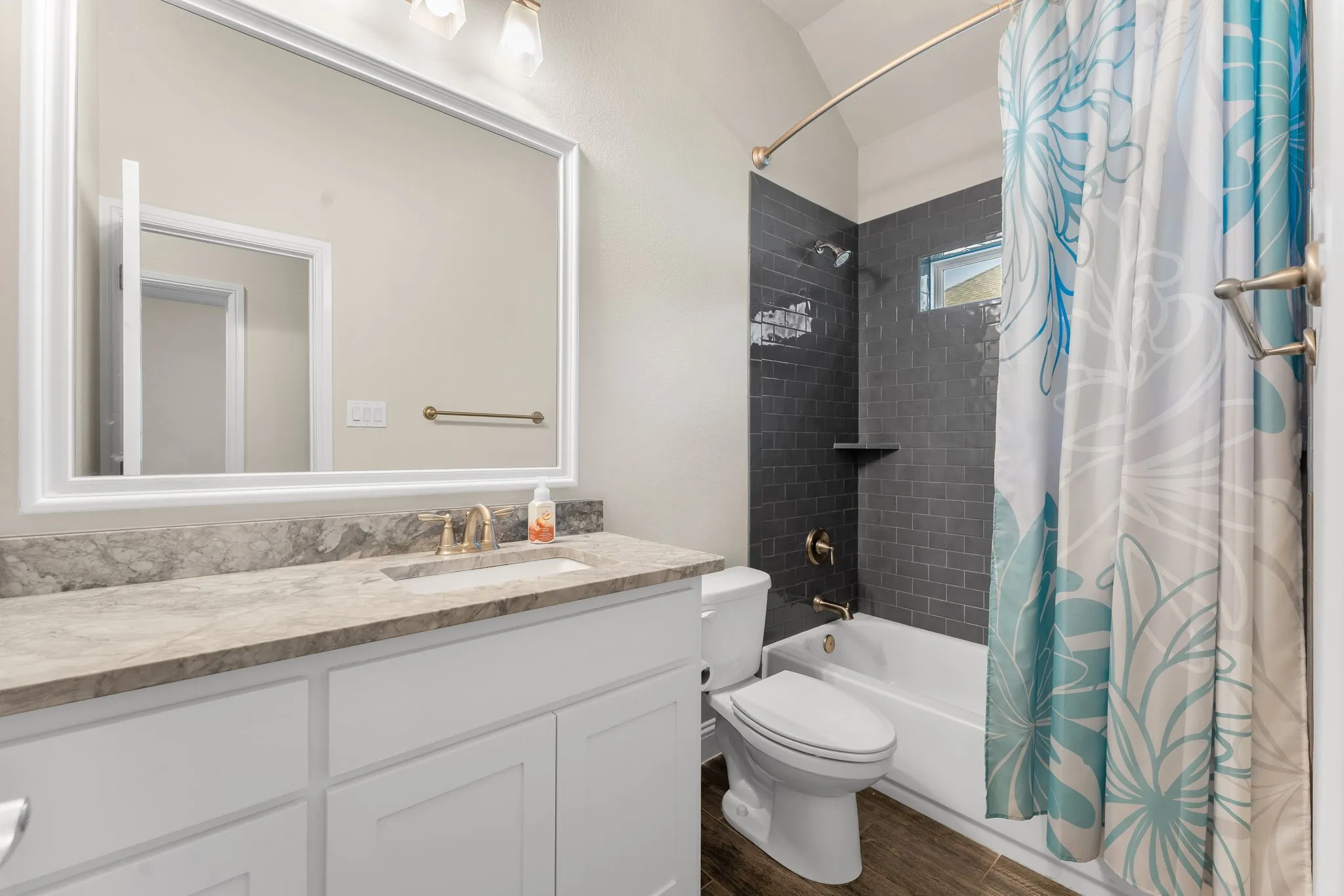 Guest bathroom with quartz countertops, tiled shower, decorative lighting, white painted cabinets, and wood tile flooring.