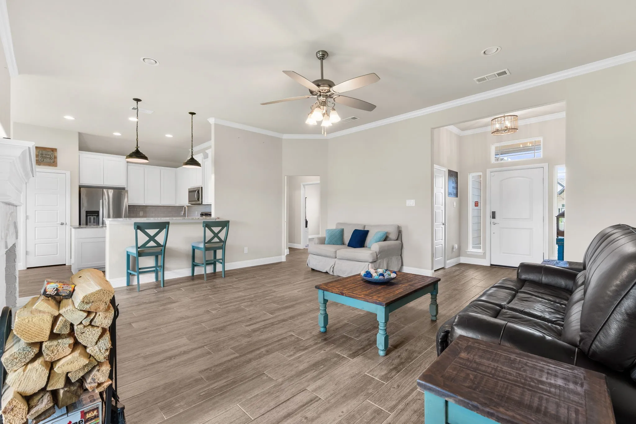 Living Room with ceiling fan, white painted brick wood burning fire place, windows for natural lighting, brown/gray wood tile flooring. Crown Moulding.
