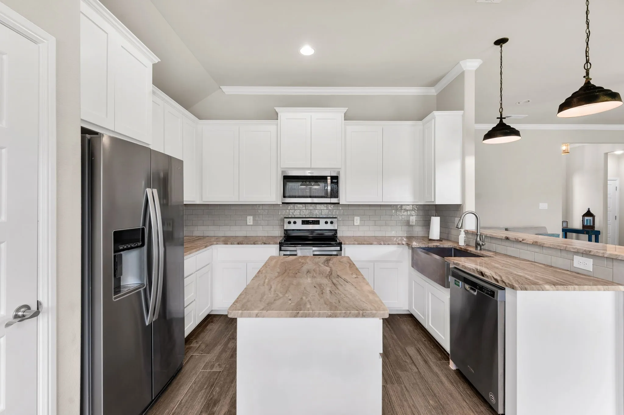 Kitchen with fresh painted white cabinets, quartz countertops, decorative breakfast bar lighting, pantry, wood tile flooring, stainless appliances.
