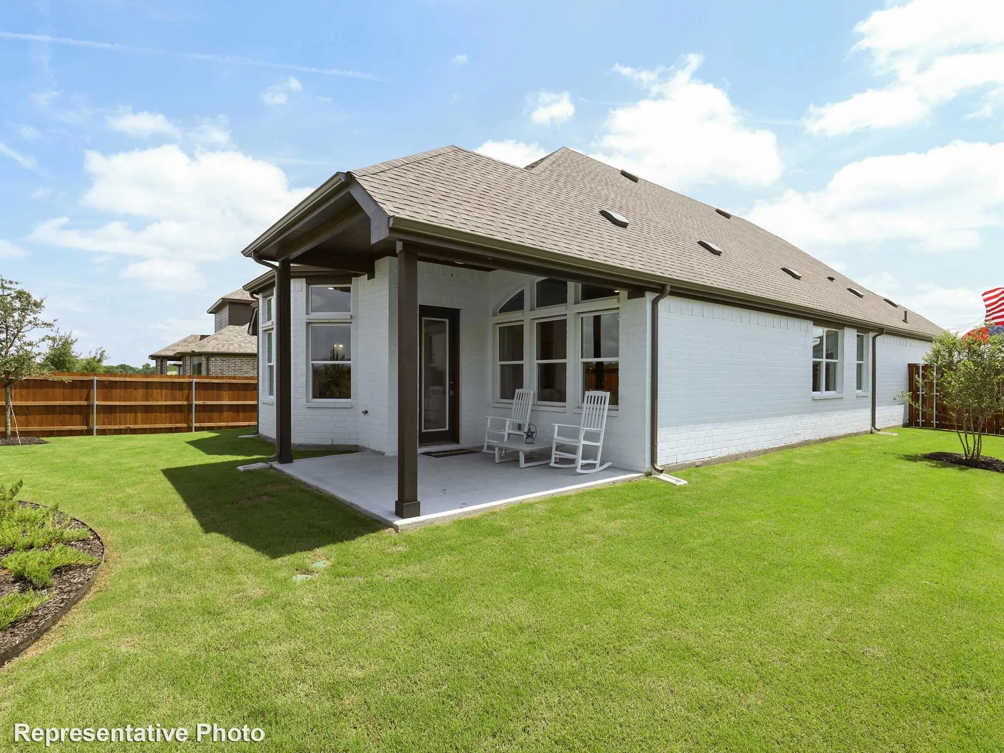 Expansive backyard featuring a manicured lawn, a covered concrete patio, white brick exterior, a full wooden privacy fence, and a pitched shingle roof