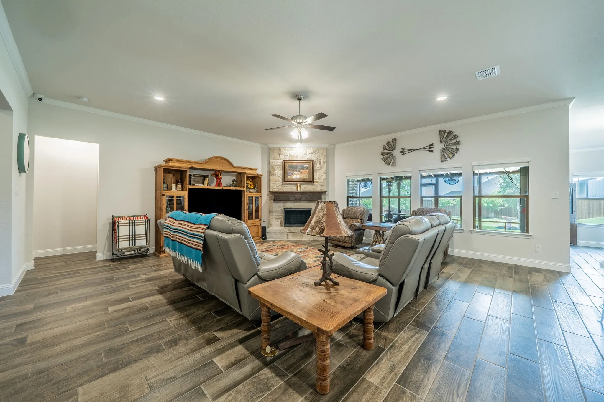 Spacious living area featuring wood-finish tile flooring, a stone fireplace with a built-in hearth, multiple windows, and a ceiling fan