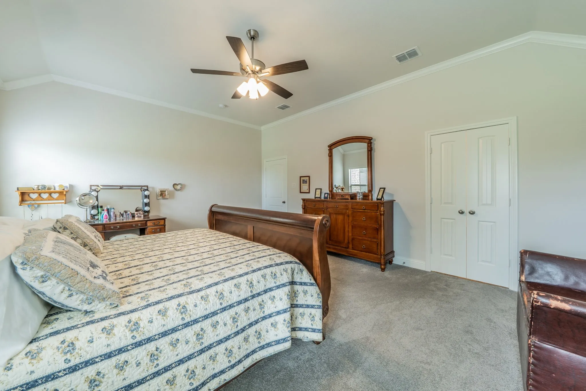 Carpeted Master Bedroom featuring a vaulted ceiling with crown molding, a ceiling fan with integrated lighting, and white bi-fold doors