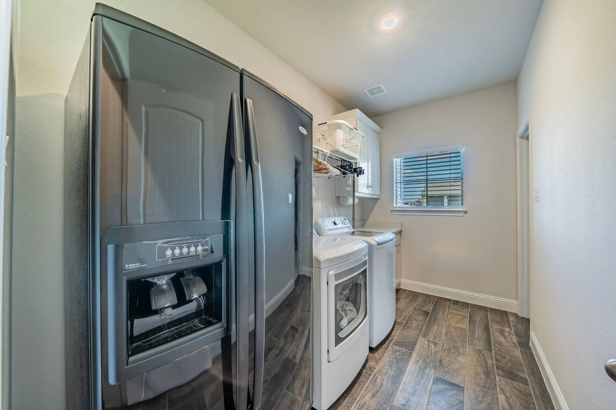 Dedicated laundry area featuring wood-finish tile flooring, a built-in countertop, white cabinetry, and a window with blinds