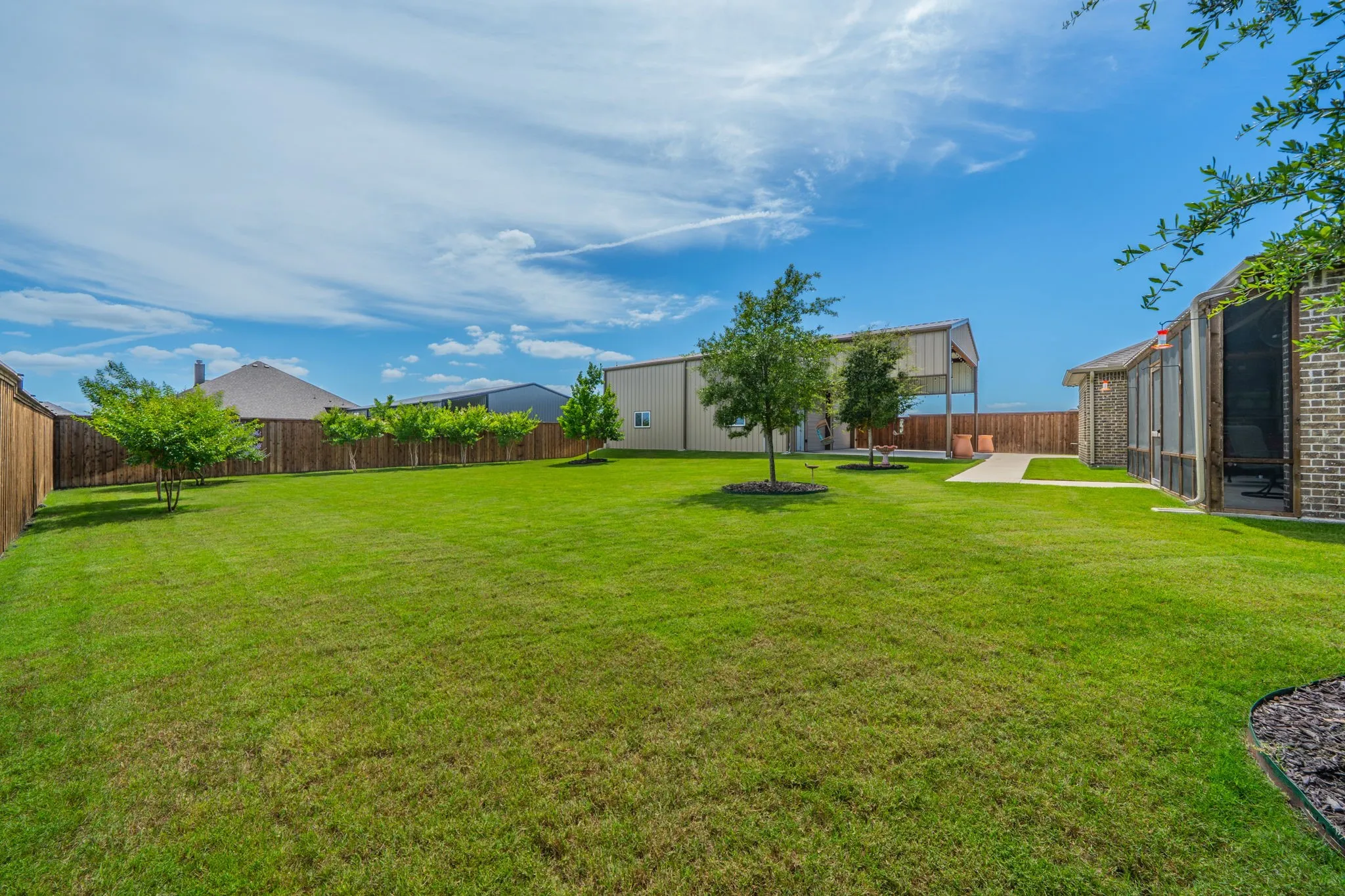 Expansive lawn area featuring mature trees, a privacy fence, and a concrete pathway leading to an open-air structure