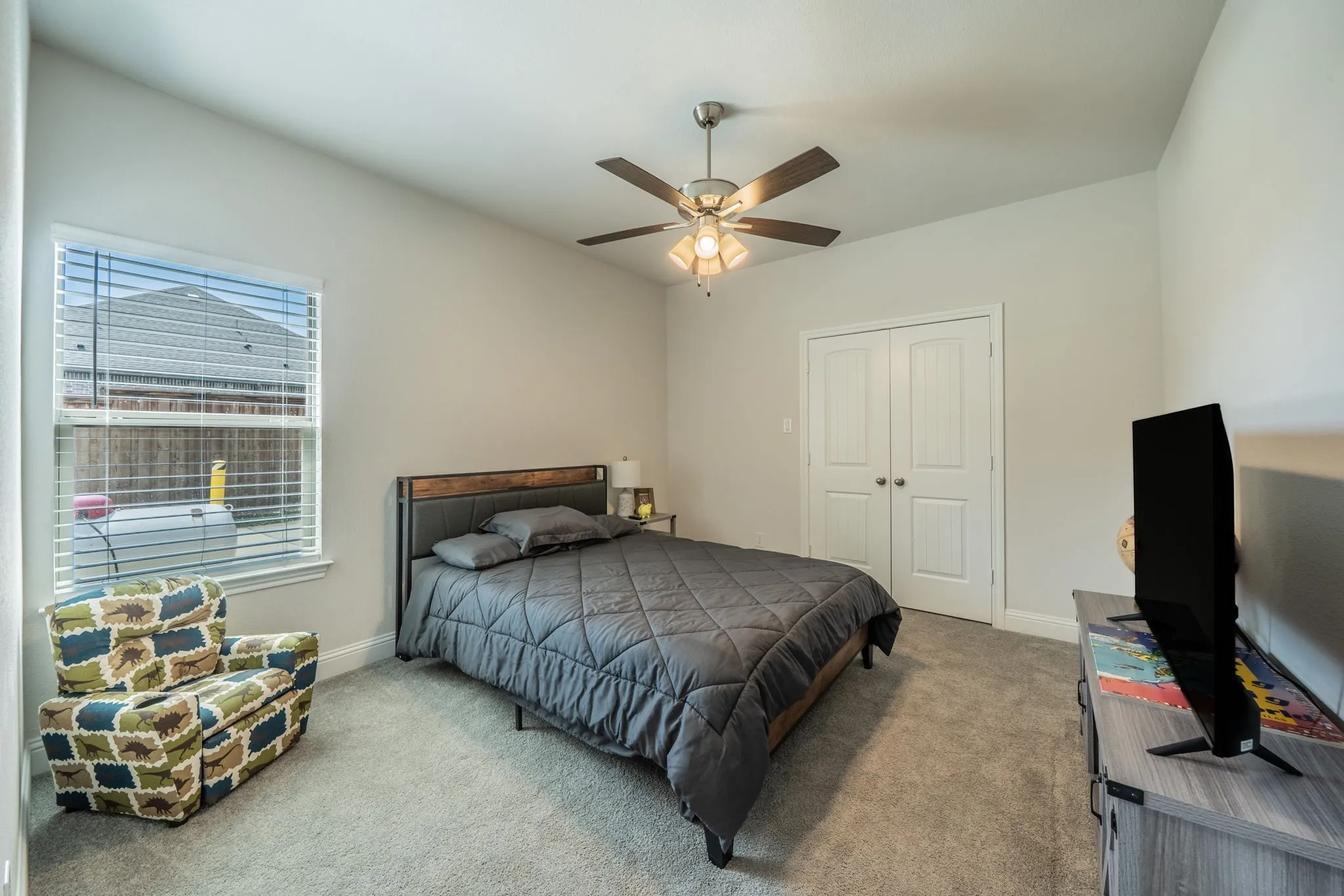 Carpeted bedroom featuring a large window with blinds, ceiling fan with integrated lighting, and double-door closet