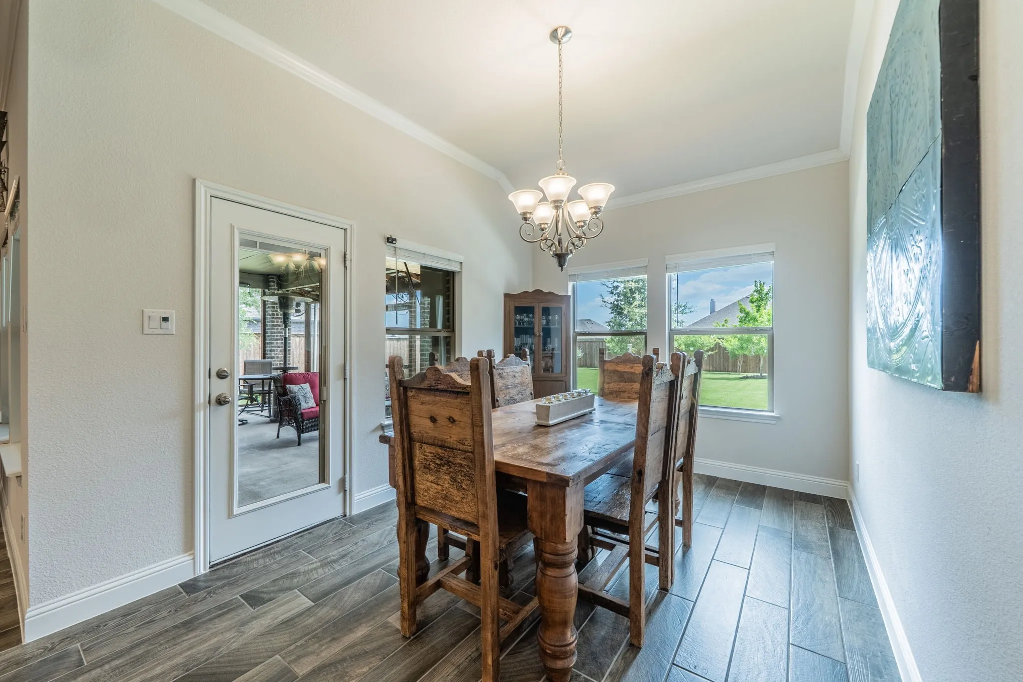 Dining area featuring wood-finish tile flooring, a glass-paneled door, two windows overlooking a backyard, and a chandelier