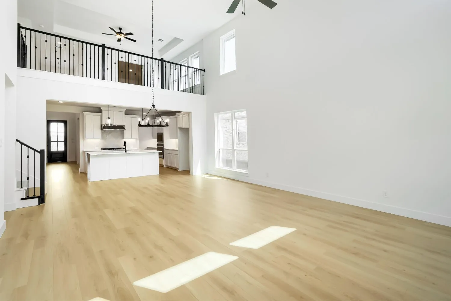 Two-story living area with wood-finish flooring, a kitchen featuring an island, and a second-story balcony with metal railings
