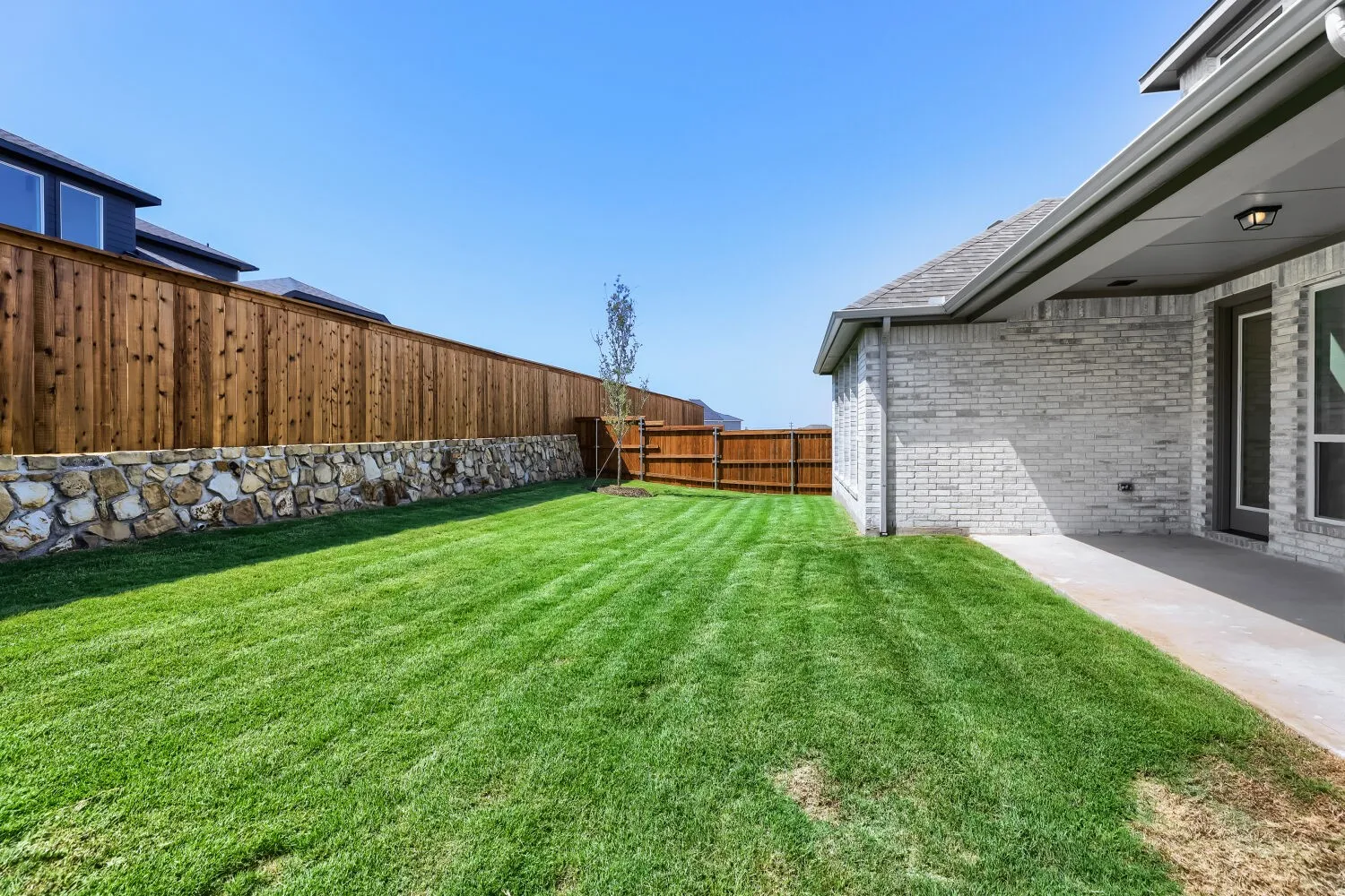 Spacious backyard featuring a manicured lawn, stone retaining wall, and a wood privacy fence