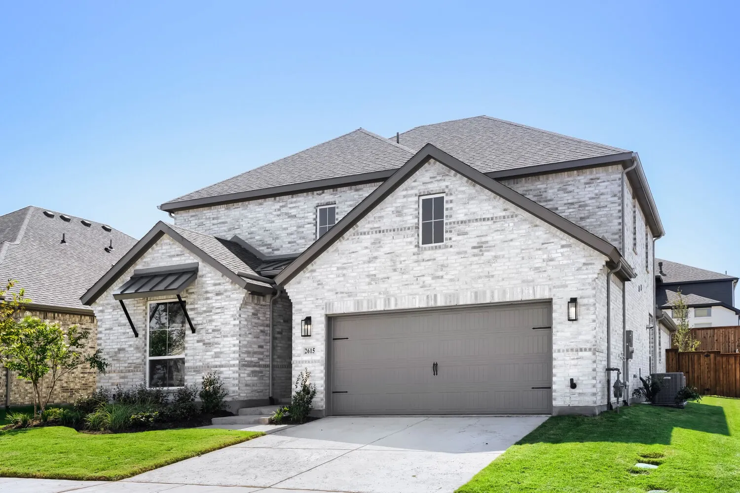 Stone brick exterior with dark trim accents, attached garage, well-maintained lawn, and a covered entry