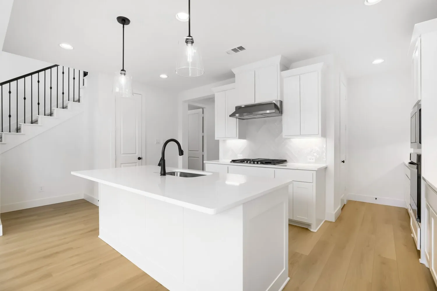 Open-concept kitchen featuring an island, white cabinetry, integrated stainless steel appliances, and light wood-finish flooring