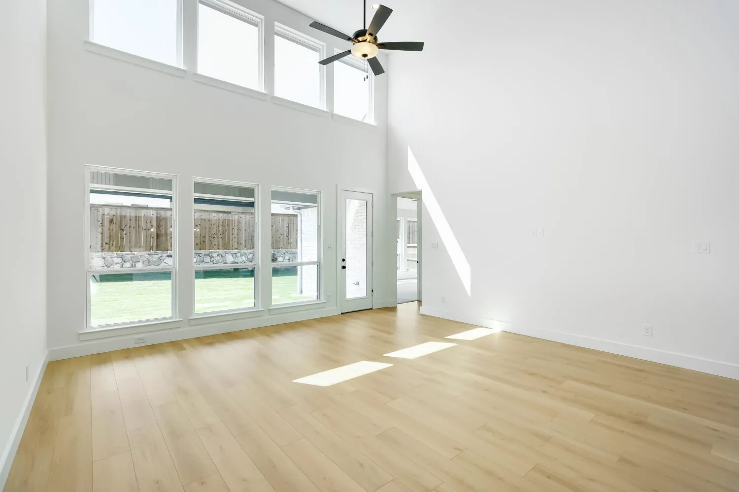 High ceilings, wood-finish flooring, abundant natural light from large windows, ceiling fan, and a glass-paneled exterior door