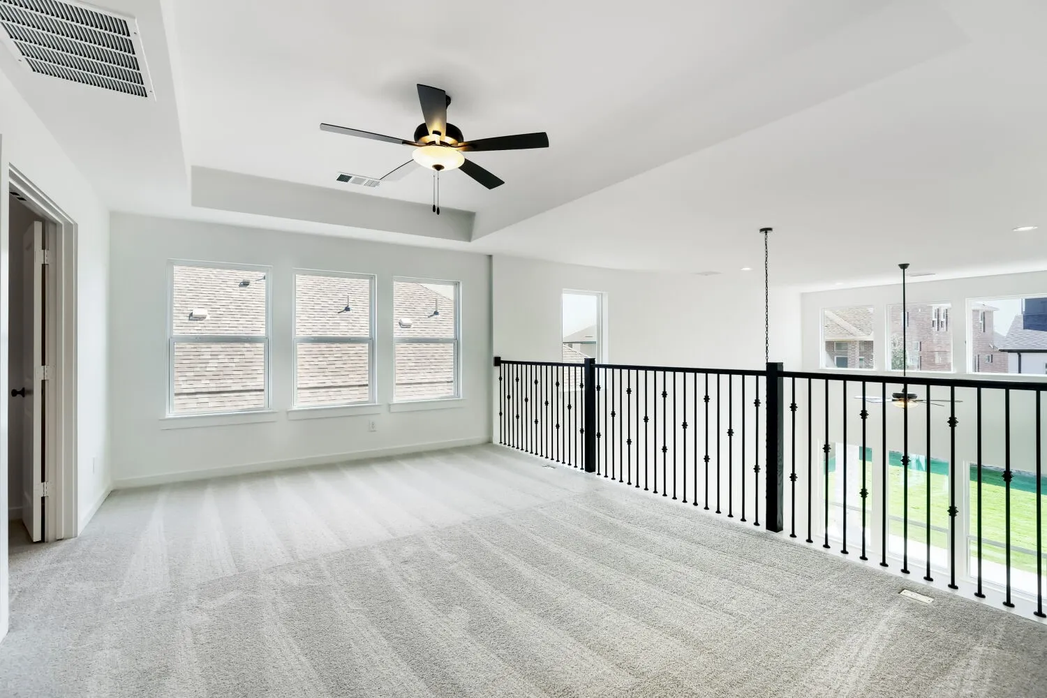 Open loft area with light gray carpeting, a tray ceiling, and a ceiling fan