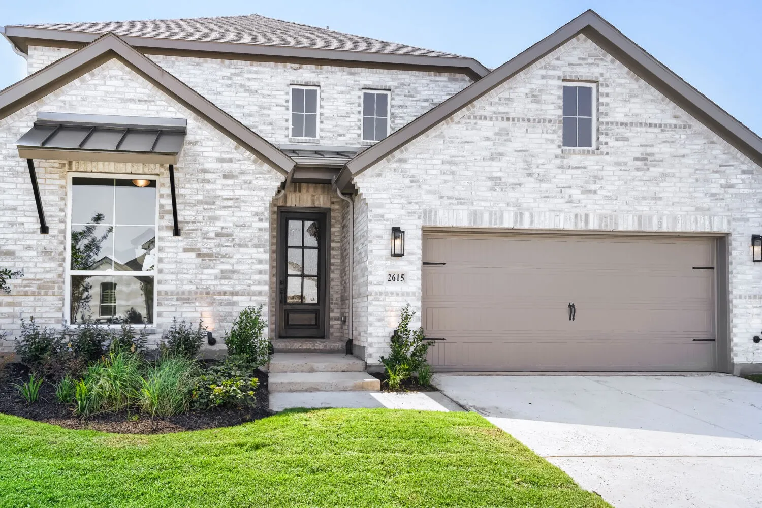 Two-story residence featuring light-colored brick masonry, an attached two-car garage, and a covered entry