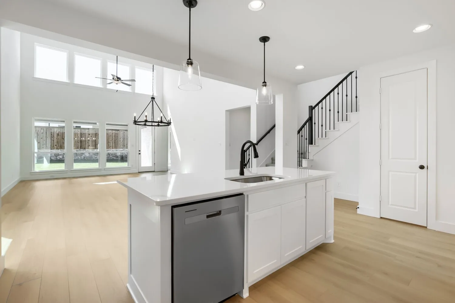 Kitchen island with white cabinetry, stainless steel dishwasher, and a white countertop with an undermount sink and black faucet