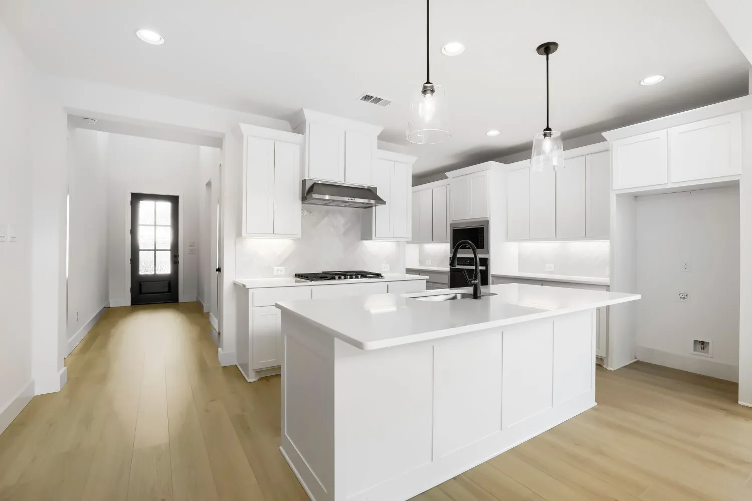 Bright kitchen with white cabinetry, a large center island, built-in appliances, and wood-finish flooring